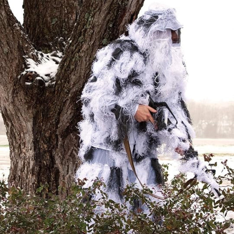 An observer in the weather-proof Arctic Snow ghillie suit, navigating a frozen forest landscape with winter tracking equipment while maintaining complete silhouette disruption.
