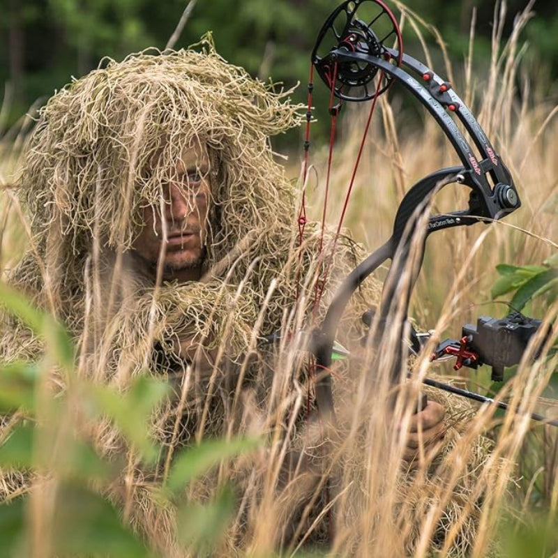 A field researcher wearing the Dry Grass ghillie suit variant, crouched in yellow-grass seasons with environmental tracking and mechanical mapping tools.