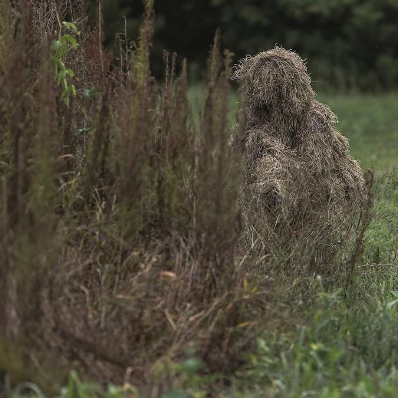 A professional wildlife photographer standing motionless in tall, dry grass to blend into a transitioning savanna or desert fringe micro-environment.