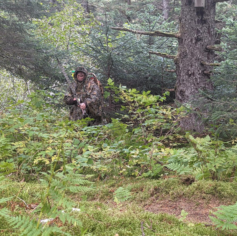 A botanical field researcher using the quick-on, quick-off GhillieLabs 3D Leafy Poncho to maintain zero-alarm proximity while sitting in low-lying alpine brush.