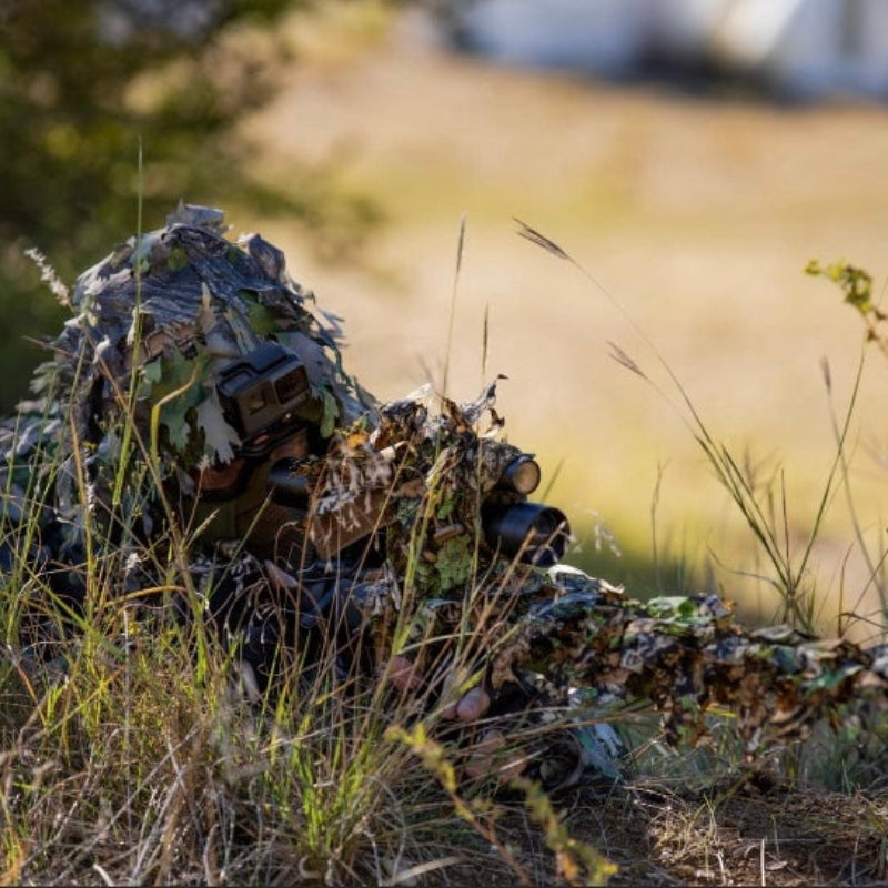 A professional observer utilizing GhillieLabs wildlife photography camouflage to shatter human silhouette while lying prone in dry autumn grasslands.