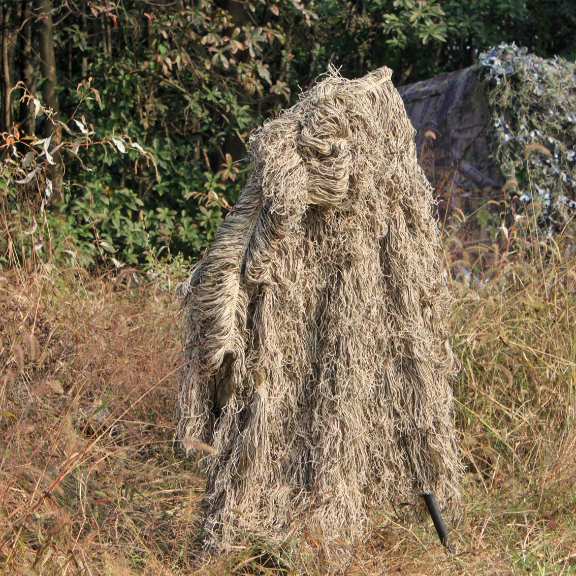 Complete visual blending of a tracker standing in tall, dry grass wearing professional ghillie gear for nature observation