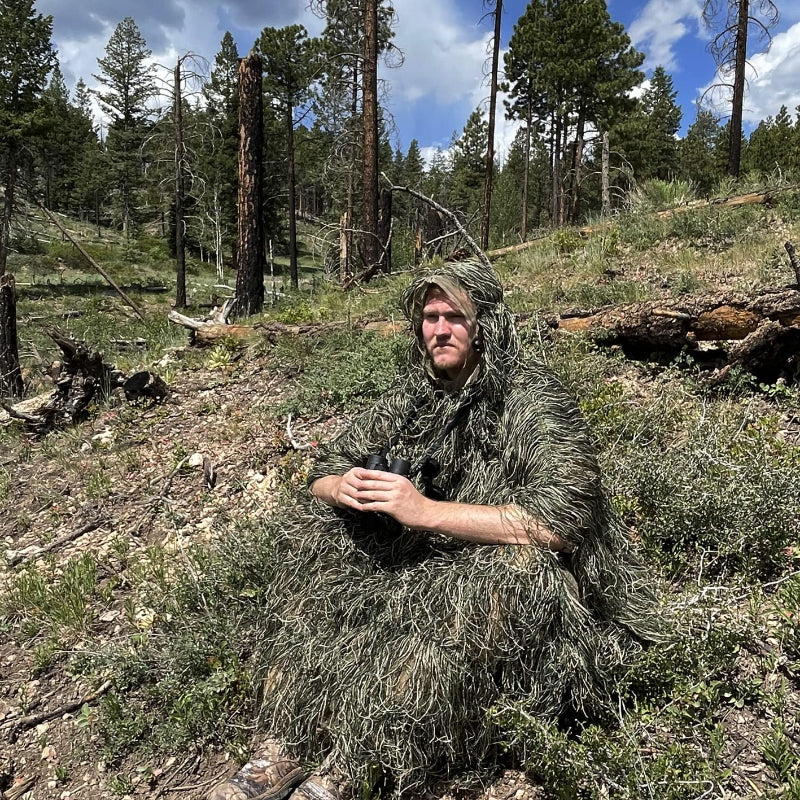 A researcher wearing the Woodland Ghost Ghillie Poncho while seated on the forest floor, demonstrating its low-noise movement