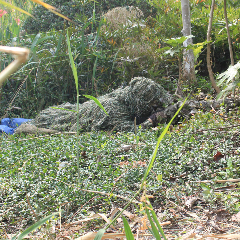 Close-up of a tracker crawling in a damp, marshy wetland with the Woodland Ghillie Poncho mimicking decaying vegetation