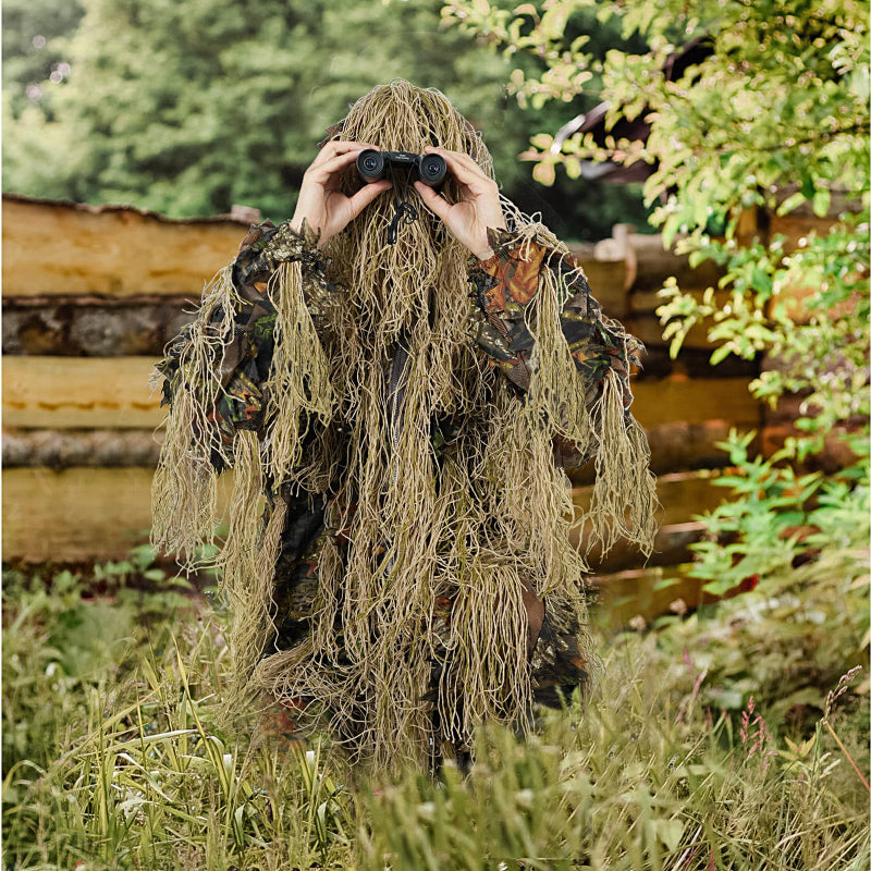 Elite nature observer utilizing the Brown Forest Hybrid Ghillie Suit while scanning a clearing with binoculars in late-season brush.